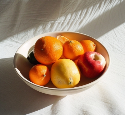 Eine Obstschale mit verschiedenen Früchten, angestrahlt vom Sonnenlicht, symbolisiert eine farbenfrohe, vitaminreiche Ernährung